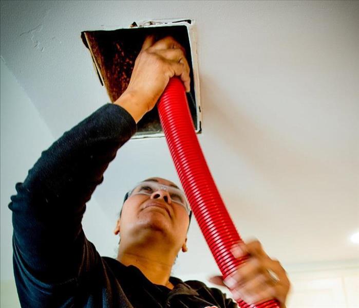 Woman cleaning air duct in ceiling.